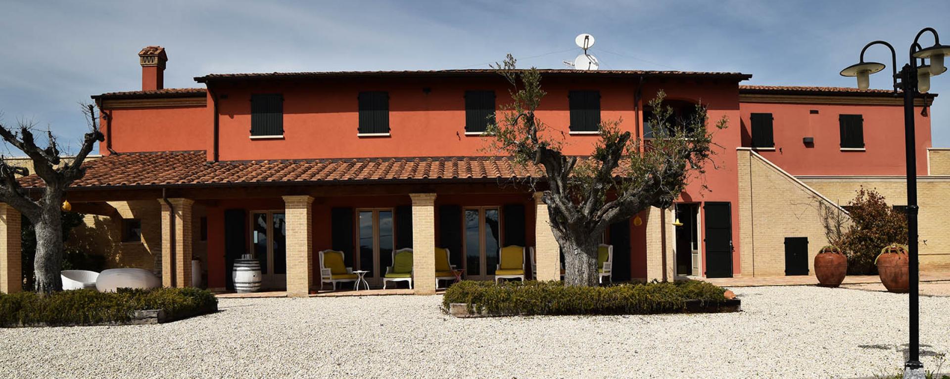 Villa rustica con pareti rosse, giardino verde, atmosfera serena e accogliente.