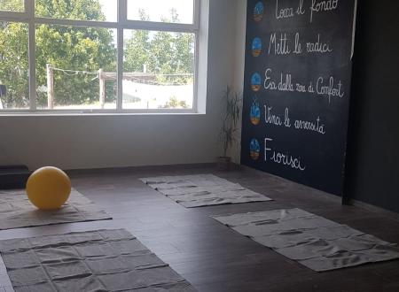 Sala yoga luminosa con tappetini, palla gialla e scritta motivazionale sulla parete.