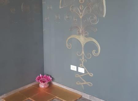 Parete grigia con disegno dorato, fiore stilizzato, piastrella dorata e fiore rosa intenso.